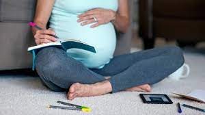 Pregnant lady holding her bump and writing a birth plan